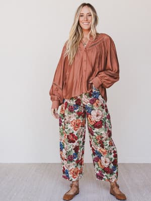 Woman wearing a rust-colored blouse and floral pants against a white background