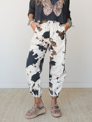 Cow print jogger pants styled with a cropped charcoal butterfly graphic sweatshirt, stacked beaded bracelets, and platform espadrille sandals — the kind of outfit that looks effortless but you absolutely thought about it.