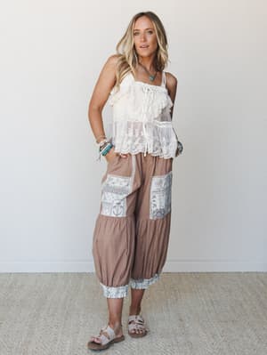 A relaxed, free-spirited look built around wide-leg harem-style pants in a warm caramel gingham check with patchwork embroidered panels and lace-trimmed cuffs, paired with a cream lace cami top and layered turquoise jewelry — the kind of outfit that