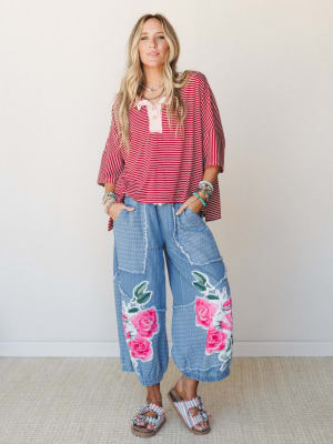 A wide-leg light denim pant with oversized rose appliqués steals the show here, paired with a boxy red striped henley top and stacked boho jewelry for a look that's equal parts playful and personal.
