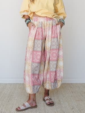 Voluminous harem-style pants in a soft bandana patchwork print styled with a buttery yellow top, stacked bracelets, and flat sandals — the kind of outfit that looks effortless but totally on purpose.