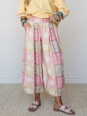 Voluminous patchwork-print harem pants in soft pink and golden tones, styled with a butter yellow sweatshirt and layered boho bracelets — the kind of outfit that looks intentional but feels like pajamas in the best way.