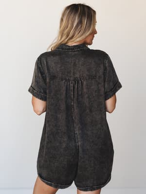A back-view shot of a relaxed mineral-washed romper in ashy black, with a soft shirt-style top and easy shorts — the kind of one-and-done piece that looks effortless without trying.