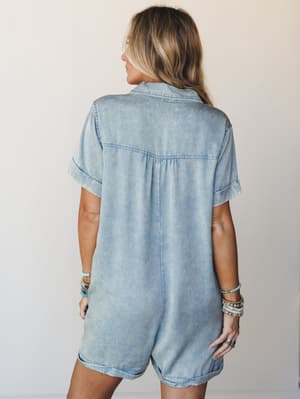 A back view of a soft, acid-washed chambray romper with a relaxed shirt-style silhouette, styled with stacked turquoise and beaded bracelets for that effortless, collected summer feel.