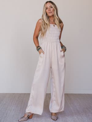 Woman wearing a light pink jumpsuit against a plain background