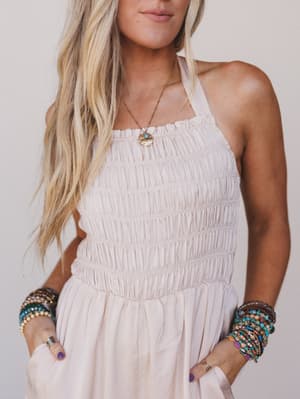 Woman wearing a white dress with colorful bracelets and a necklace against a plain background