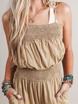 Woman wearing a beige smocked top and skirt with colorful bracelets on a neutral background