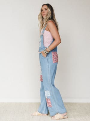 A wide-leg light denim overall jumpsuit styled with a pink lace cami and strappy sandals — the patchwork details in pink tweed and crochet give it that collected, one-of-a-kind feel that looks effortless rather than try-hard.