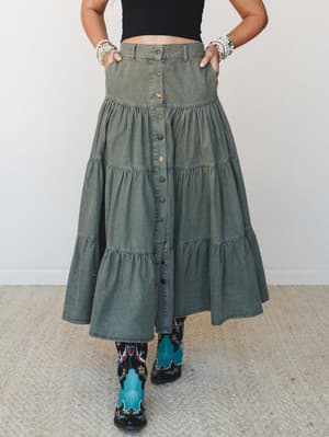 An olive washed-denim tiered maxi skirt styled with a black crop top and bold printed cowboy boots — the kind of outfit that hits the farmers market in the morning and a honky-tonk by night.