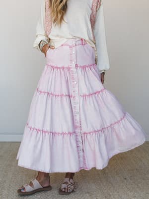 A breezy pink acid-wash tiered maxi skirt styled with a cream floral-sleeve top and flat sandals — the kind of outfit that feels intentional without trying too hard.