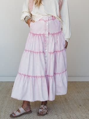 A tiered maxi skirt in washed pink denim styled with a cream oversized top and neutral sandals — the kind of easy, feel-good outfit that works just as hard at a farmers market as it does at a backyard birthday.