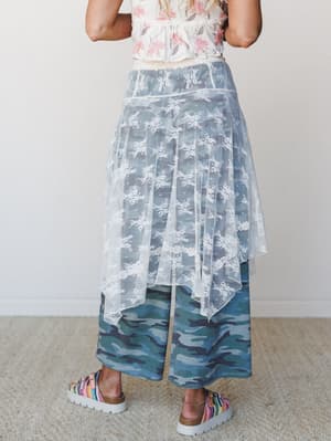 Shot from the back, this layered look pairs a sheer cream lace overlay skirt with wide-leg camo pants and a floral smocked top — an unexpected mix that somehow works, soft and a little rule-breaking.