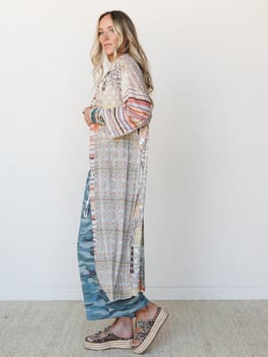A floor-length patchwork duster in a mix of floral, stripe, and camo prints styled with stacked turquoise bracelets and platform espadrille sandals — the kind of piece that looks like it has a story.