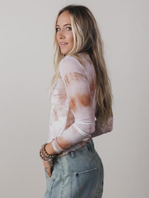 Woman wearing a sheer top with a pattern and high-waisted jeans against a plain background