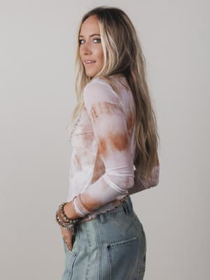 Woman wearing a sheer top with a pattern and high-waisted jeans against a plain background