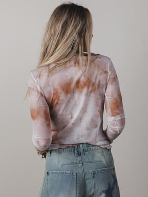 Person wearing a tie-dye shirt and jeans against a plain background
