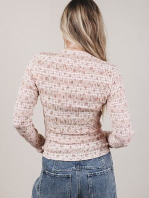 Person wearing a textured pink top and blue jeans against a plain background