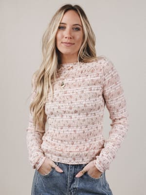 Woman wearing a pink textured sweater and blue jeans against a plain background