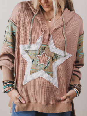 Person wearing a pink hoodie with a star design on a plain background