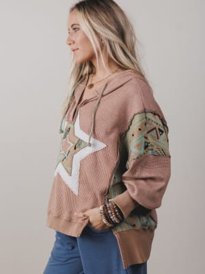 Woman wearing a patterned hoodie with geometric designs on a plain background