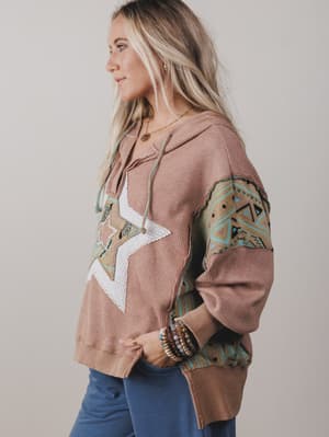 Woman wearing a patterned hoodie with geometric designs on a plain background
