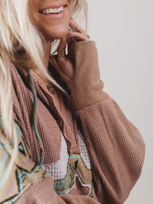 Person wearing a brown textured jacket with a patterned garment underneath on a plain background