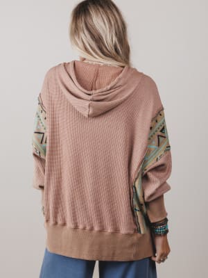 Person wearing a pink hoodie with patterned sleeves on a plain background