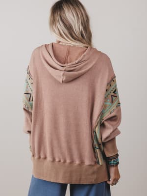Person wearing a pink hoodie with patterned sleeves on a plain background
