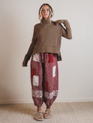 Woman wearing a brown turtleneck sweater and patterned pants against a plain background