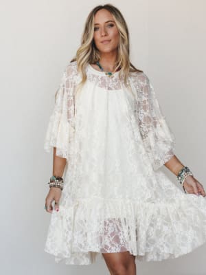 A flowy cream lace mini dress with flutter sleeves and a ruffled hem, styled with stacked boho bracelets and a turquoise beaded necklace — the kind of dress that works just as hard at a bridal shower as it does twirling at a summer festival.