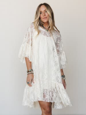 A cream lace mini dress with flutter sleeves and a ruffled hem styled with layered turquoise and beaded jewelry — effortlessly romantic and made for someone who dresses like a feeling.