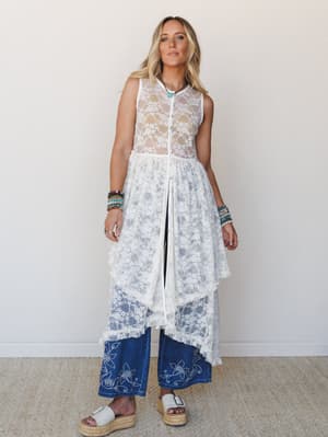 A sheer cream lace maxi duster layered over wide-leg embroidered denim — the kind of outfit that feels like it was thrown together perfectly, styled with stacked beaded bracelets, a turquoise necklace, and espadrille platform sandals against a soft n
