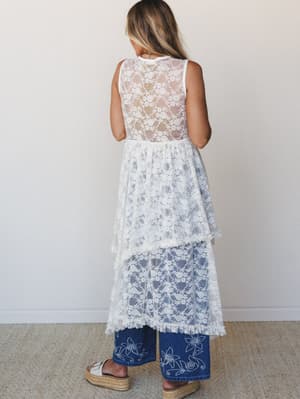 Shot from the back, this layered cream lace dress worn over wide-leg embroidered jeans captures that effortlessly romantic mix of soft and structured — the sheer floral lace skimming over denim feels intentional, not accidental.