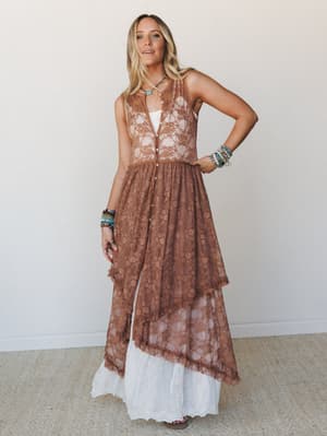 A sheer mocha lace duster layered over a white maxi skirt, styled with stacked beaded bracelets and a turquoise pendant — the kind of outfit that looks like it was thrown on effortlessly but absolutely wasn't.