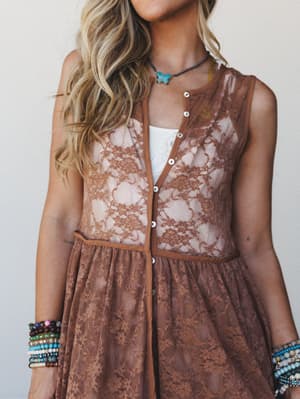 A sheer mocha lace button-front dress layered over a white tank, styled with stacks of beaded bracelets and a turquoise stone choker — the kind of outfit that looks effortless but took exactly the right amount of thought.
