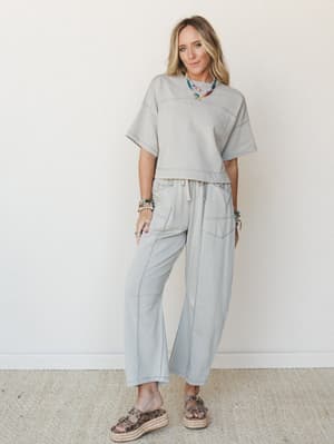 A relaxed matching set in washed dove grey — oversized crop tee and wide-leg drawstring pants styled with colorful beaded necklaces and leopard platform sandals, giving off that effortlessly put-together energy.