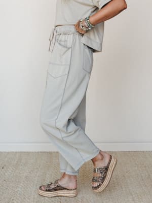 A side-profile shot of relaxed dove grey jogger pants styled with a matching cropped tee, stacked beaded bracelets, and leopard print platform sandals — effortlessly put-together in that 'running errands but make it intentional' kind of way.