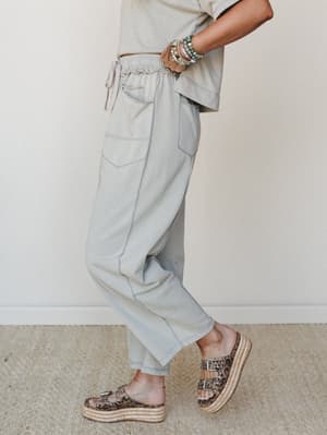 A side-profile shot of relaxed dove grey jogger pants styled with a matching cropped tee, stacked beaded bracelets, and leopard print platform sandals — effortlessly put-together in that 'running errands but make it intentional' kind of way.