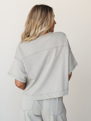 A soft, washed-grey matching set shot from the back — the boxy crop top and wide-leg pants move together in that effortless way that makes you want to wear them everywhere from a coffee run to a beach boardwalk.