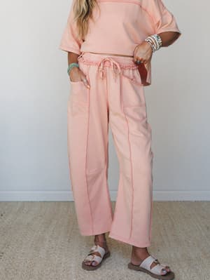 A matching peach-coral wide-leg pants and cropped tee set styled with buckle sandals and layered turquoise and pearl bracelets — relaxed, soft, and the kind of outfit that looks effortless on a slow Saturday.