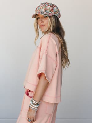 A relaxed, lived-in matching set in soft coral pink styled with a floral newsboy cap and a full stack of beaded bracelets — the kind of outfit that looks effortless but was definitely thought about.