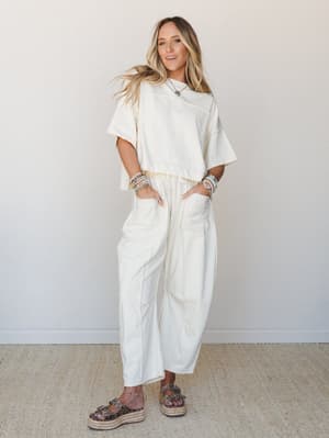 A cream matching set — oversized crop tee and relaxed barrel-leg pants with a drawstring waist — styled with stacked bead bracelets, a turquoise pendant necklace, and platform leopard sandals for an effortlessly put-together everyday look.