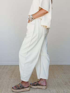A side-profile shot of cream wide-leg barrel pants paired with a matching oversized tee, styled with leopard print platform sandals and a stack of beaded bracelets — relaxed and put-together at the same time.