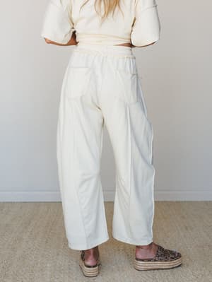 A back-view shot of cream wide-leg pants with patch pockets and a braided elastic waistband, styled with a matching cropped tee and leopard print platform espadrilles — relaxed and put-together at once.