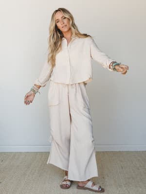 A breezy, tonal cream set — cropped button-down shirt and wide-leg drawstring pants in a soft gauze fabric — styled with sandals and layered boho jewelry for an effortlessly relaxed feel.