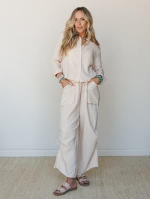 A breezy matching set in soft blush-cream gauze — button-down top and wide-leg pants styled with stacked turquoise bracelets and slide sandals, giving off that effortlessly pulled-together energy.
