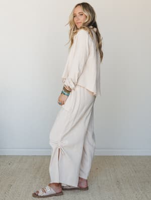 A cream gauze matching set — oversized button-down top and wide-leg maxi pants with a ruched side detail — styled with stacked beaded bracelets and buckle sandals for that effortless, lived-in feel.