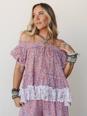 A flowy off-shoulder floral set in soft lilac and red ditsy print, styled with stacked beaded bracelets and a turquoise pendant necklace — the kind of outfit that looks like it was pulled together effortlessly but definitely wasn't.
