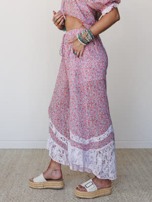 A side-profile shot of a flowy floral-print maxi skirt with a lace hem detail, styled as a two-piece set with stacked beaded bracelets and white platform espadrille sandals — soft, romantic, and effortlessly boho.