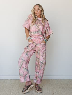 A matching pink camo two-piece set styled with stacked beaded bracelets and platform sandals — playful and relaxed with just enough personality to make the whole look feel intentional.